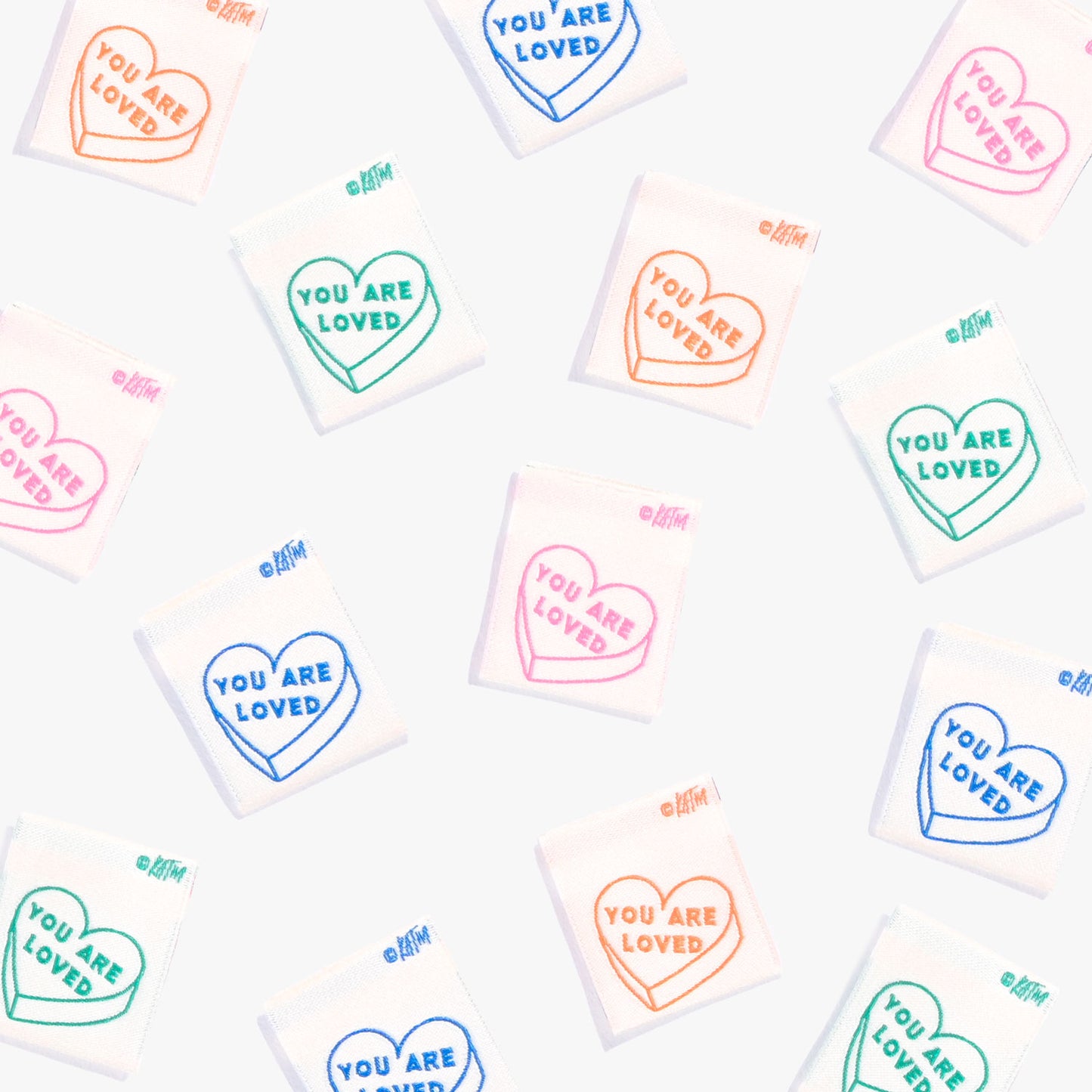 Labels van Kylie and the Machine verspreid op een witte achtergrond. Op de labels staan hartjes en de tekst 'You are Loved' in de kleuren blauw, groen, roze en oranje.